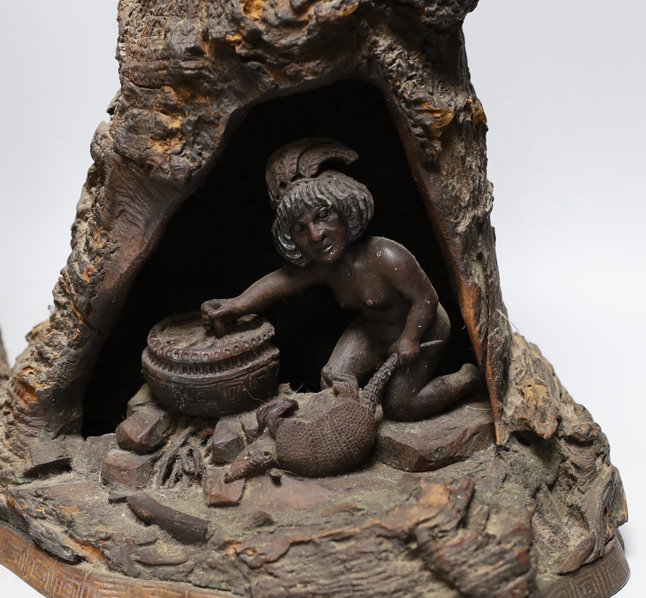 A wood carving of a bear climbing amongst rocks and a tree and another similar carving of figure cooking inside a cave, 40cms high